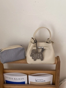 Cream white pebble leather bucket bag with horse charm and striped pouch on shelf