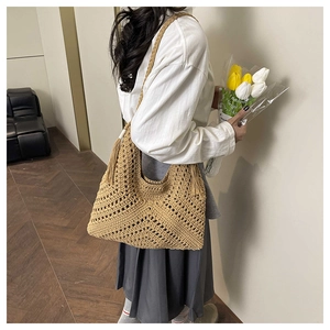 Detail of hand-woven straw shoulder bag with hollow V-pattern and side tassel accents