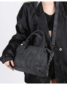 Close-up of black Boston handbag with textured leather, round handles and shoulder strap