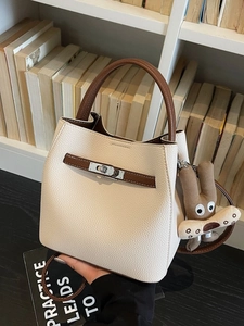 Chic beige bucket bag with brown leather handles and a playful rabbit charm on black surface