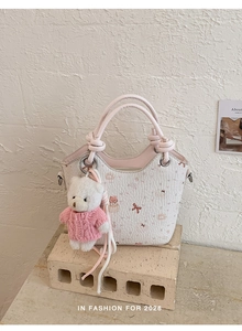 Detail of printed bucket bag featuring cartoon pattern and teddy bear charm on cream bricks