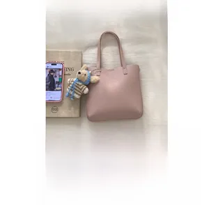 Pink lychee grain leather bucket bag with a striped bear charm in a lifestyle setting