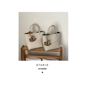 Détail d'un sac seau en cuir beige grainé avec charmant pendentif en bois de cheval