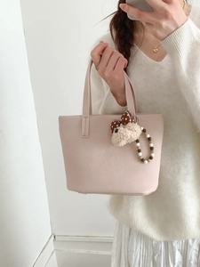 Detail of pink leather bucket bag with plush charm and beaded strap held by model