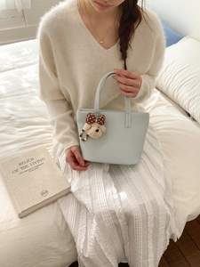 Pale blue pebbled leather bucket bag with cute bear charm held by model in white outfit