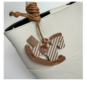 Detail of horse-shaped leather charm with white stripes on a cream-colored bucket bag