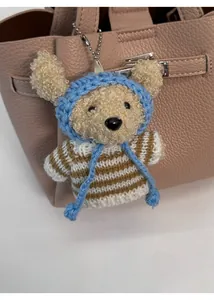 Détail d'un charm ours en peluche bouclée avec pull rayé et bonnet bleu sur un sac
