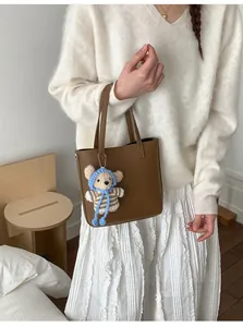 Brown lychee grain leather bucket bag featuring a cute knitted bear charm on a white sweater