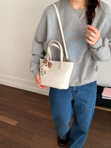 Close-up of cream leather bucket bag with cute teddy bear charm and crossbody strap
