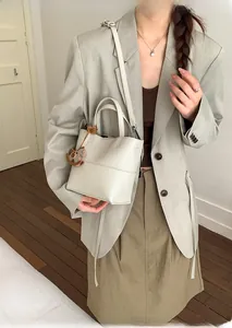 Chic cream lychee grain leather bucket bag styled with a grey blazer and brown charm