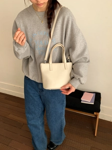 Close-up of cream leather bucket bag with top handles and slender shoulder strap
