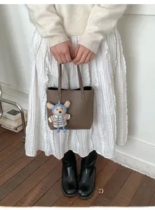 Detail of a brown lychee pattern bucket bag with a cute bear charm on a wood floor