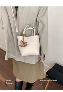 Model wearing a cream white grainy leather tote bag with a small horse charm