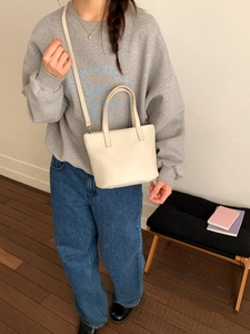 Chic cream bucket bag shown as a crossbody on a model with casual daily outfit