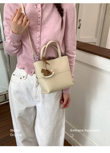 Close-up of off-white lychee grain leather handbag with a wooden rocking horse charm