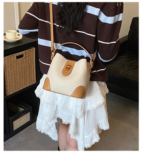 Detail of cream bucket bag with brown trim and gold lock worn by a model in lifestyle setting