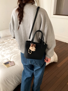 Detail of black tote bag with cute plush puppy charm and adjustable shoulder strap