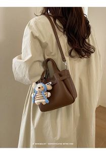 Détail du sac à main en cuir marron foncé avec breloque ours et bandoulière réglable