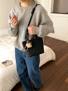 Detail of a black minimalist bucket bag with a plush bear charm held by a model