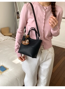 Gros plan sur un sac seau noir en cuir grainé avec un pendentif cheval en bois élégant