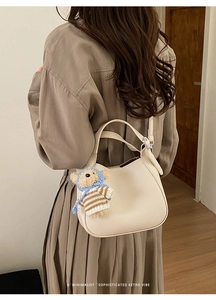 Beige litchi grain bucket bag with matching strap and cute bear pendant on a model