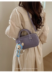 Detail of purple crossbody bag with bear pendant and embossed logo on casual sweater