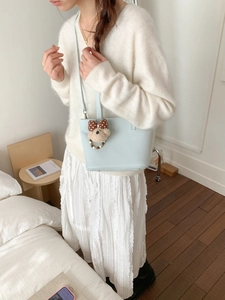 Detail of light blue bucket bag with cute plush bear charm on white knitted outfit