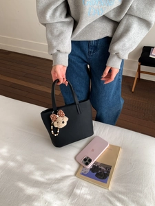 Detail of black pebbled leather bucket bag featuring a cute plush bear and bow charm