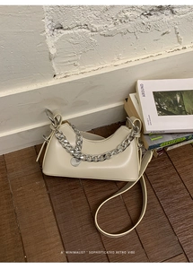 Borsa sottobraccio beige minimalista con catena argento su pavimento in legno