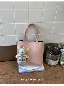 Pink lychee grain leather bucket bag with cute teddy bear charm on minimalist wooden setup