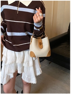 Detail of minimalist cream leather bucket bag with contrast brown trim and golden clasp
