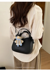 Detail view of black litchi leather bucket bag featuring a cute teddy bear charm pendant