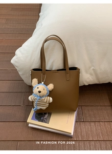 Detailed view of a brown pebbled leather tote bag with a cute bear plush charm on books