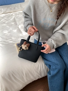 Close-up of black textured leather bucket bag featuring a cute plush bear charm detail