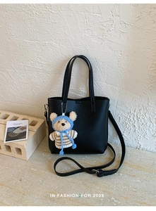 Detailed close-up of a black lychee leather tote bag with a cute bear plush pendant