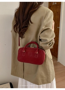 Detail of red vintage suede tote bag with embossed logo and gold zipper on a model