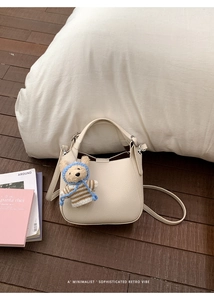 Detail view of cream bucket bag with litchi texture and cute bear charm on wood