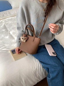 Close-up of brown leather bucket bag with a cute plush bear charm on soft white bedding