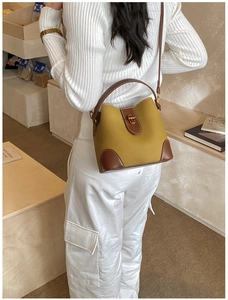 Detail of mustard yellow bucket bag with brown leather trim and golden twist lock