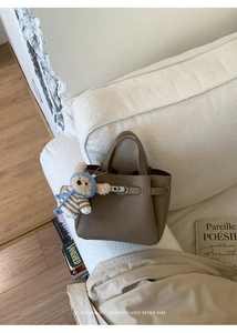 Détail d'un sac cabas en cuir marron avec un charm ours en peluche posé sur un canapé blanc