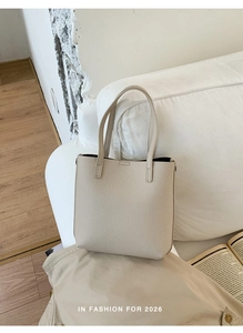 Detailed close-up of light beige lychee pattern leather bucket bag on white sofa