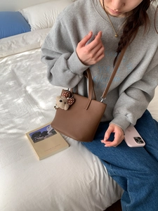 Brown leather bucket bag with cute bear charm shown in a casual lifestyle setting