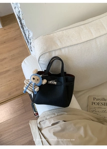 Détail du sac seau en cuir noir à grain litchi avec un charmant pendentif d'ours