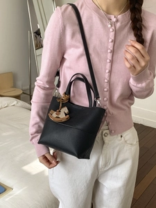 Sac seau chic en cuir grainé noir avec charme cheval en bois, porté par un mannequin en intérieur