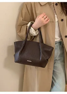 Détail de sac cabas en cuir marron foncé avec plaque logo argentée de style vintage