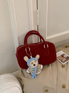 Sac à main minimaliste en daim rouge foncé avec pendentif ours sur un trench-coat