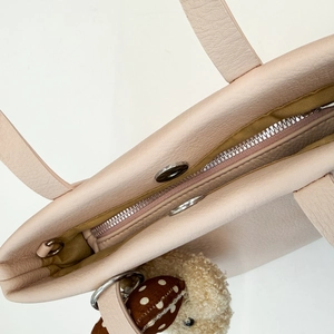 Detail of light pink pebble leather bucket bag with metal zipper and cute bear charm
