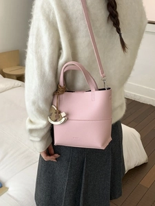 Sac seau rose en cuir grainé avec breloque cheval, porté par un mannequin chic
