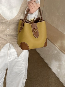 Mustard yellow bucket bag with brown leather trim and golden metal swivel lock closure