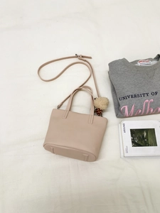Detail of cream bucket bag with strawberry plush charm and adjustable strap on fabric
